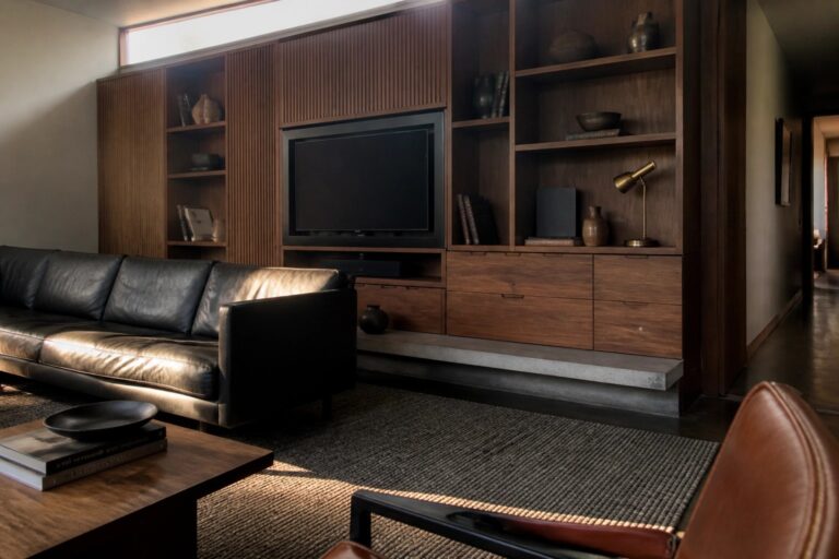 21 Clever Masculine Interior Design Ideas for Built-In Storage and Display A living room with a large wooden built-in entertainment center featuring open shelves, a television, drawers, and a dark leather sofa positioned in front.