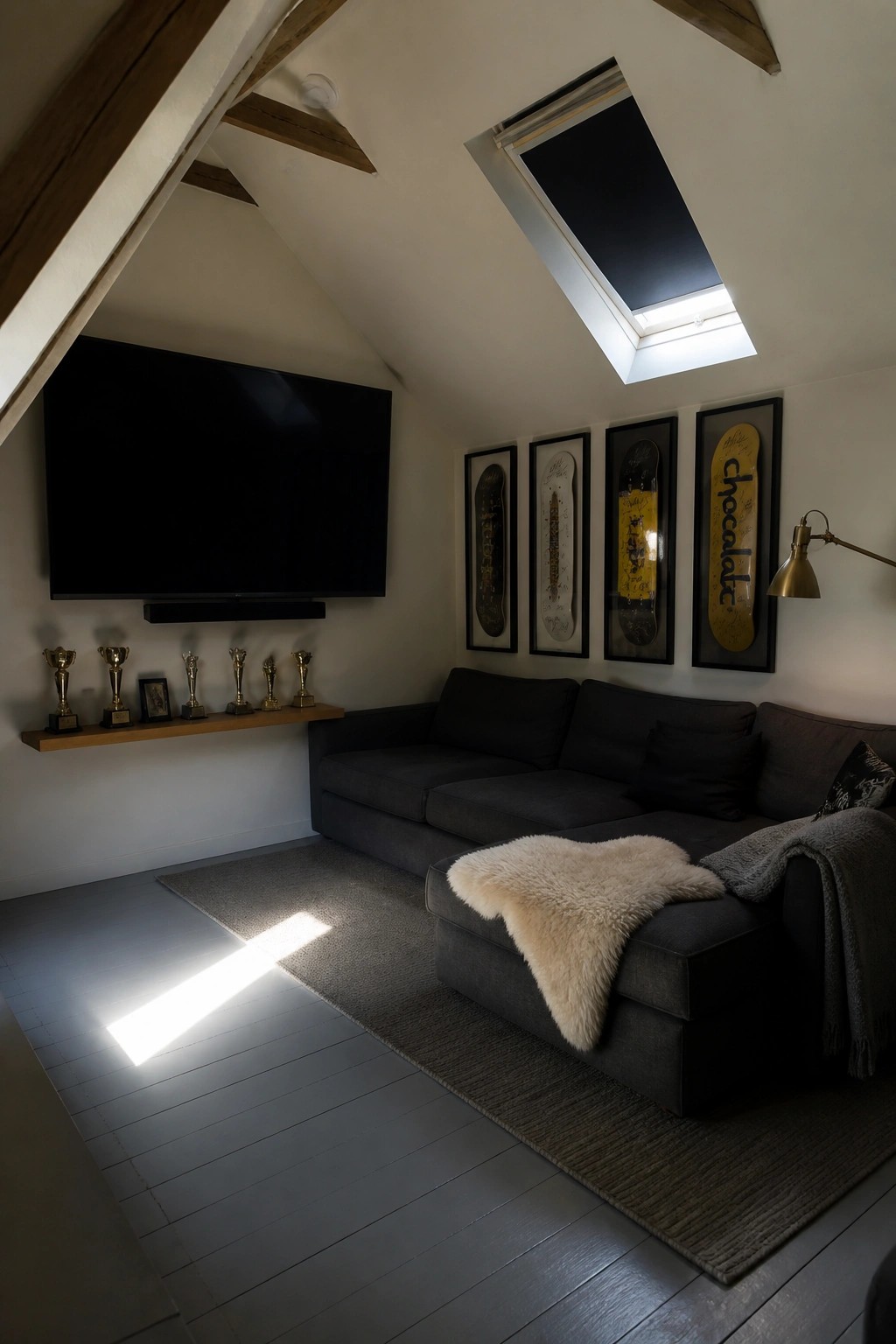 Attic lounge with dark sectional sofa, wall-mounted TV, framed skateboards, and skylight.
