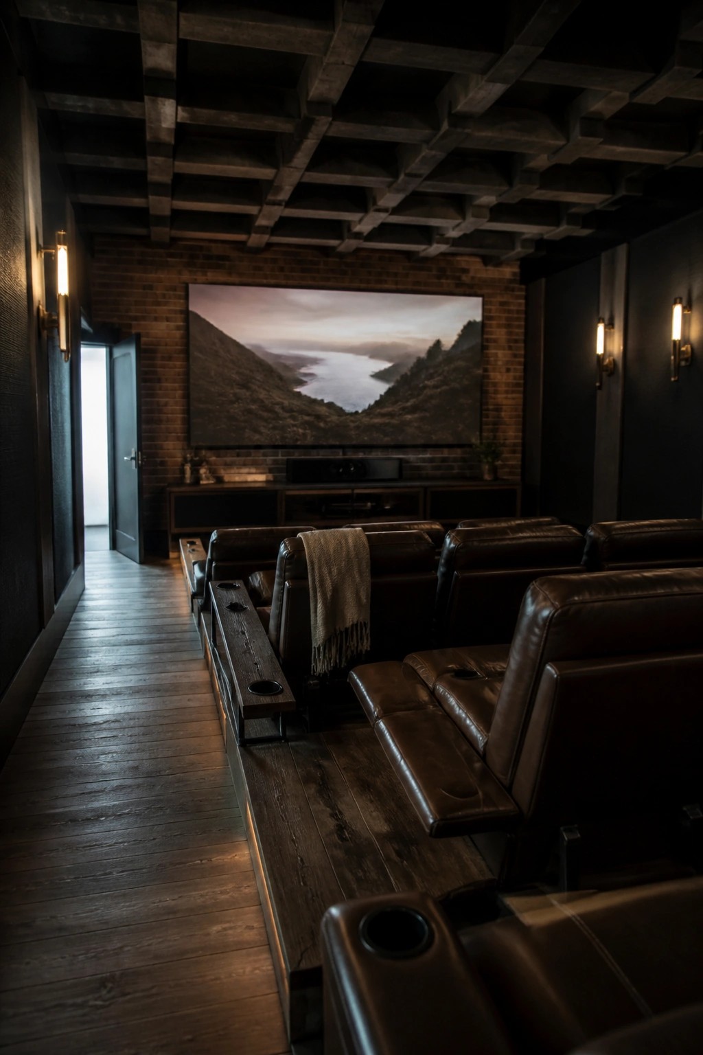 A dimly lit home theater with brown leather recliners arranged in rows facing a large screen on an exposed brick wall, dark wood ceiling, and wall sconces.