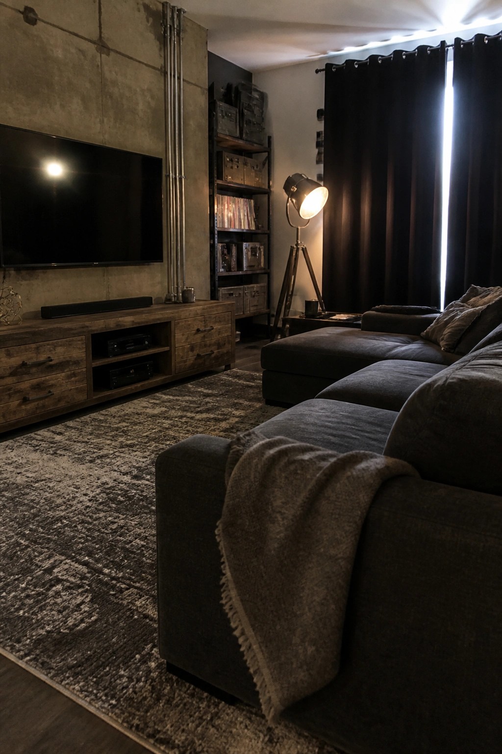 Dimly lit living room with dark sectional sofa, wooden TV console, and tripod floor lamp.
