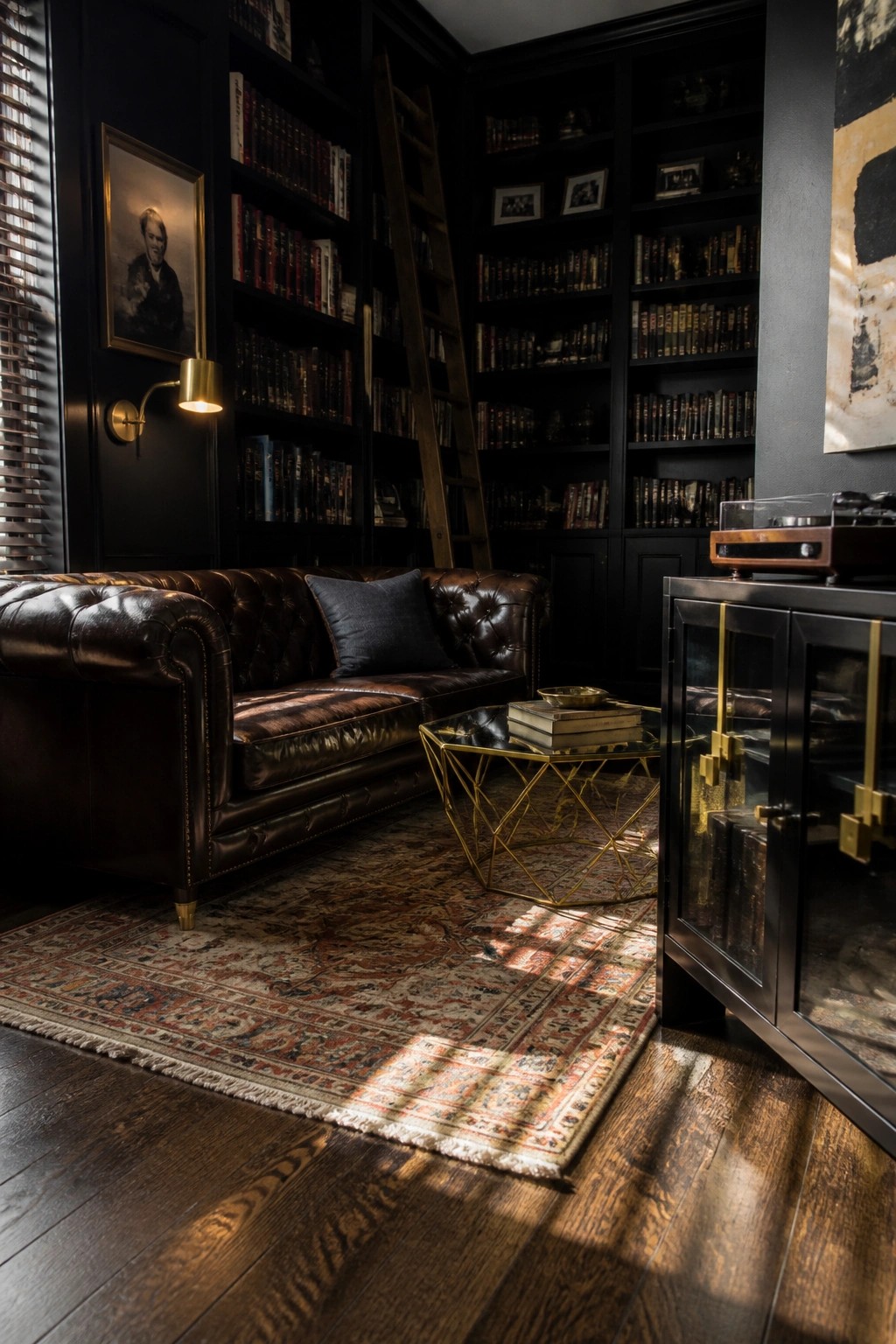 Interior view of a dark library with built-in bookshelves, brown leather sofa, geometric brass coffee table, and patterned rug on wood floors.