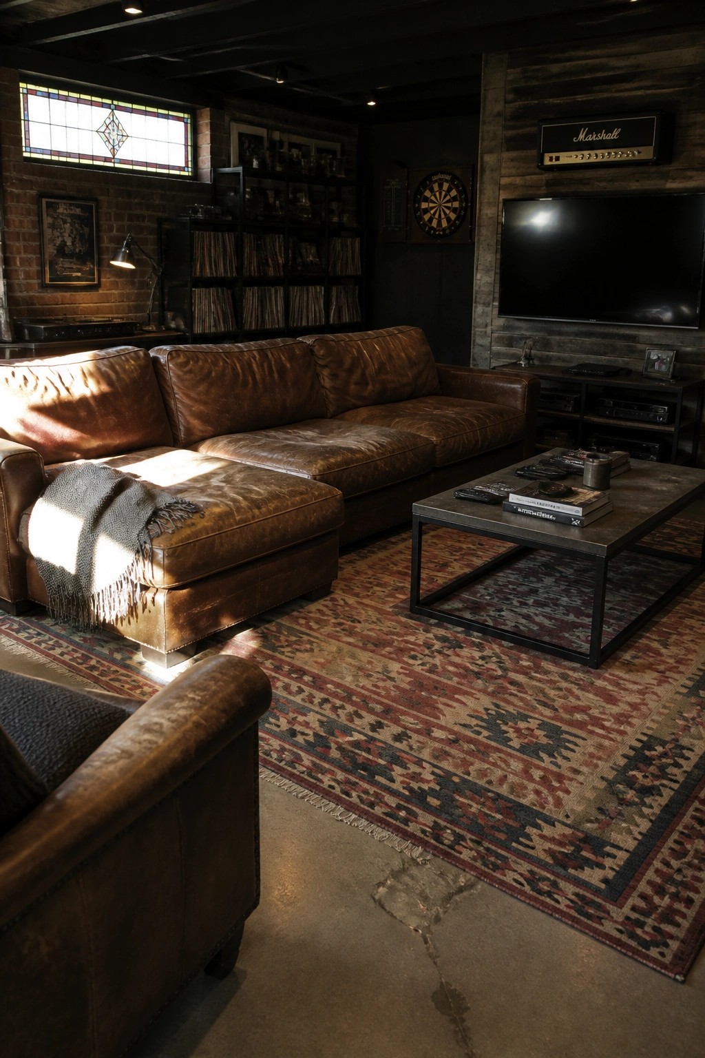 A man cave interior with a large brown leather sectional sofa, patterned rug, coffee table, wall-mounted TV, and wood-paneled accent wall.