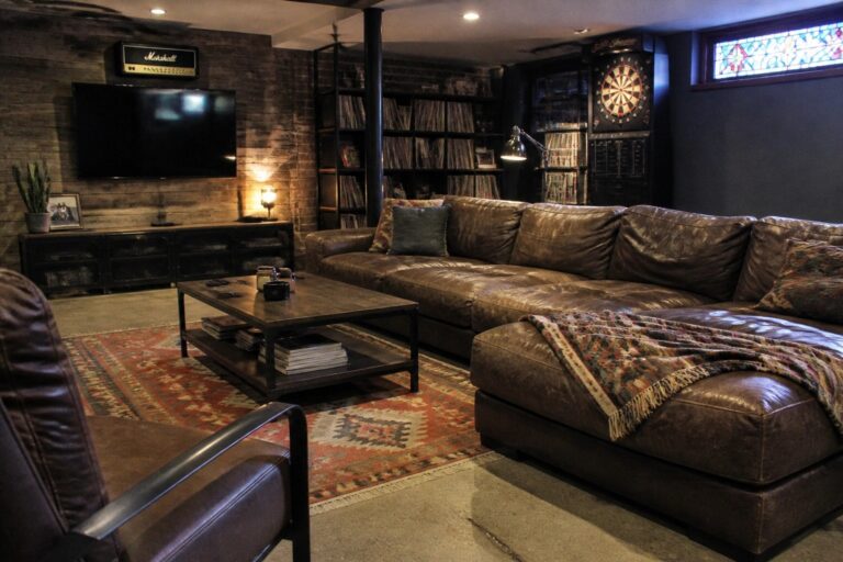 24 Bold Man Cave Ideas Built Around Oversized Lounge Seating A man cave interior with a large brown leather sectional sofa, patterned rug, coffee table, wall-mounted TV, and wood-paneled accent wall.