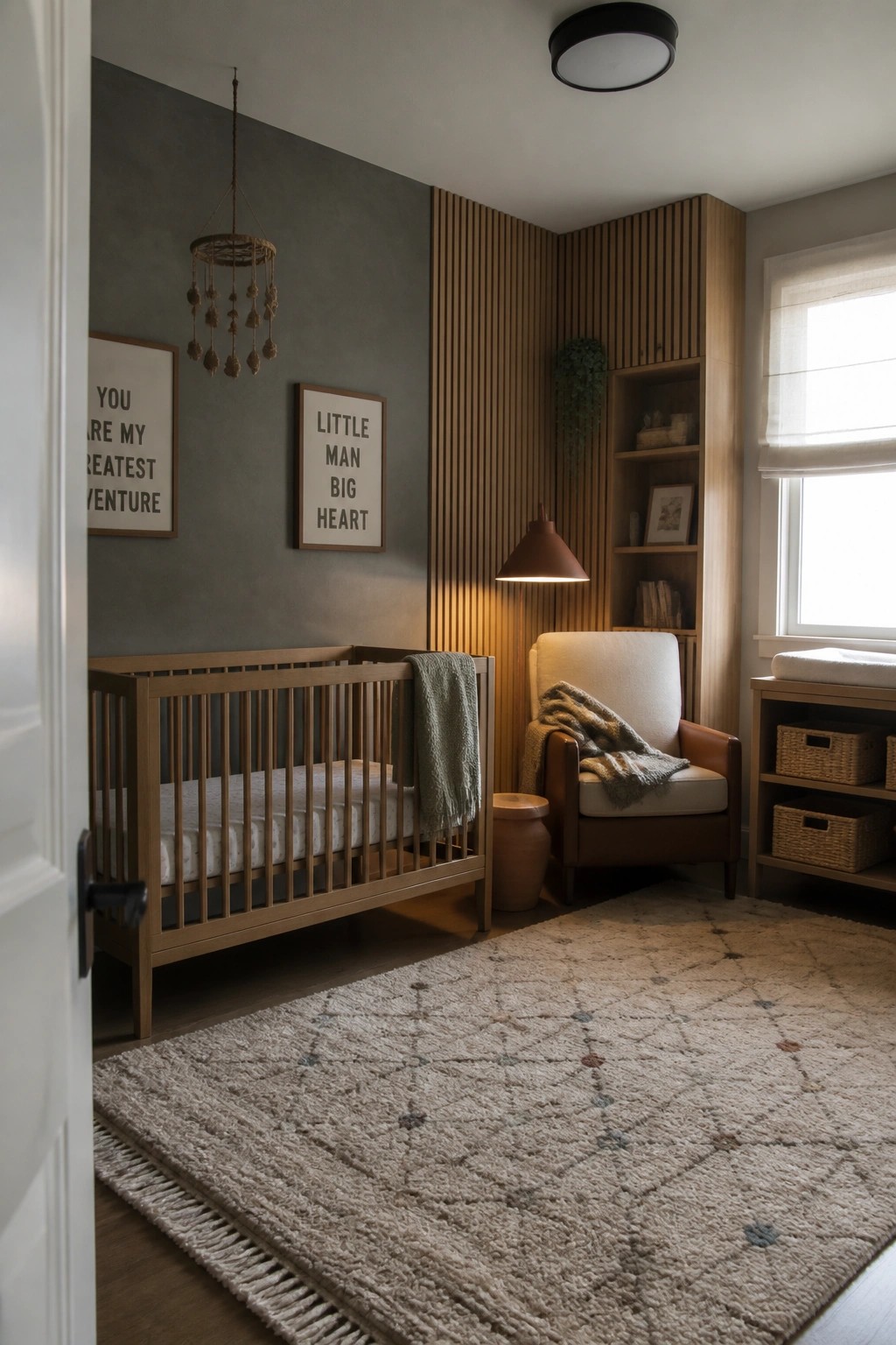A nursery interior with a wooden crib on the left, an upholstered armchair with a side table and lamp, built-in shelving on a fluted wood wall, and a large patterned rug on the floor.