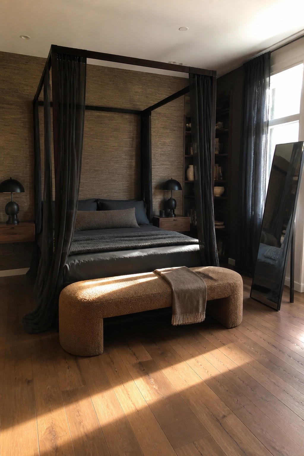 A bedroom with a dark wooden canopy bed draped in sheer black curtains, a brown upholstered bench at the foot of the bed, and a tall mirror near a window.
