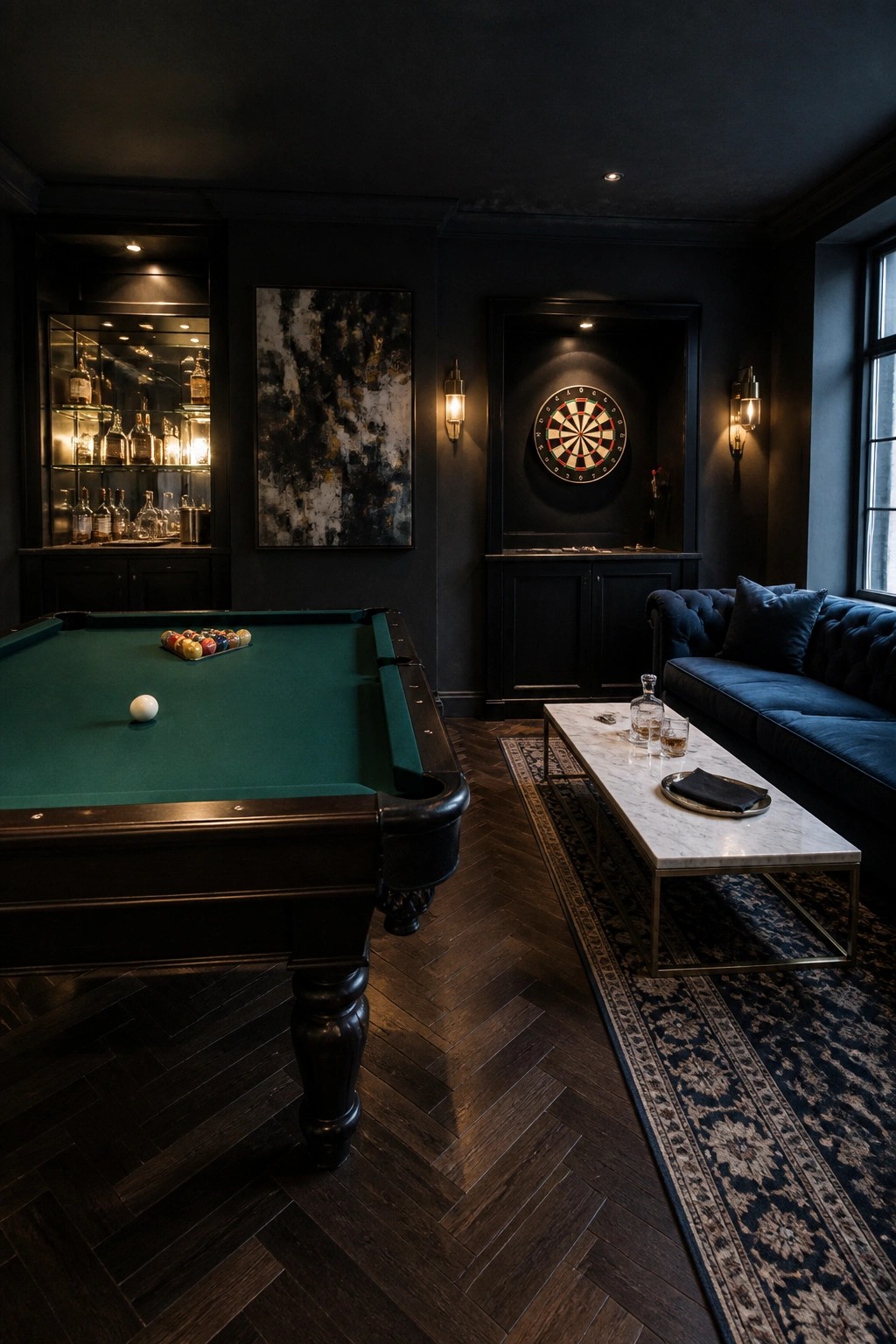 A dimly lit game room with a green felt pool table, a dartboard recessed in a dark wall niche, a blue velvet sofa, and a marble coffee table on a patterned rug.