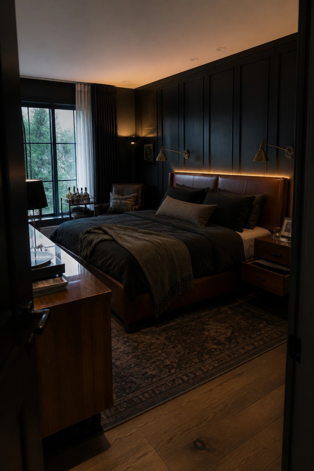 Dark moody bedroom with leather bed, black linens, wood paneling, and warm sconces.