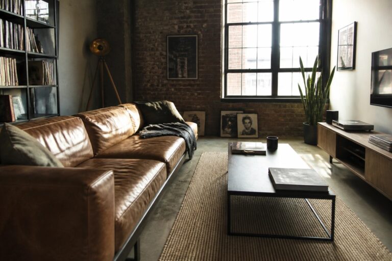 24 Stylish Masculine Living Room Ideas Centered Around Low-Profile Seating A living room featuring a low brown leather sofa, black coffee table on a woven rug, large windows, and a brick wall.