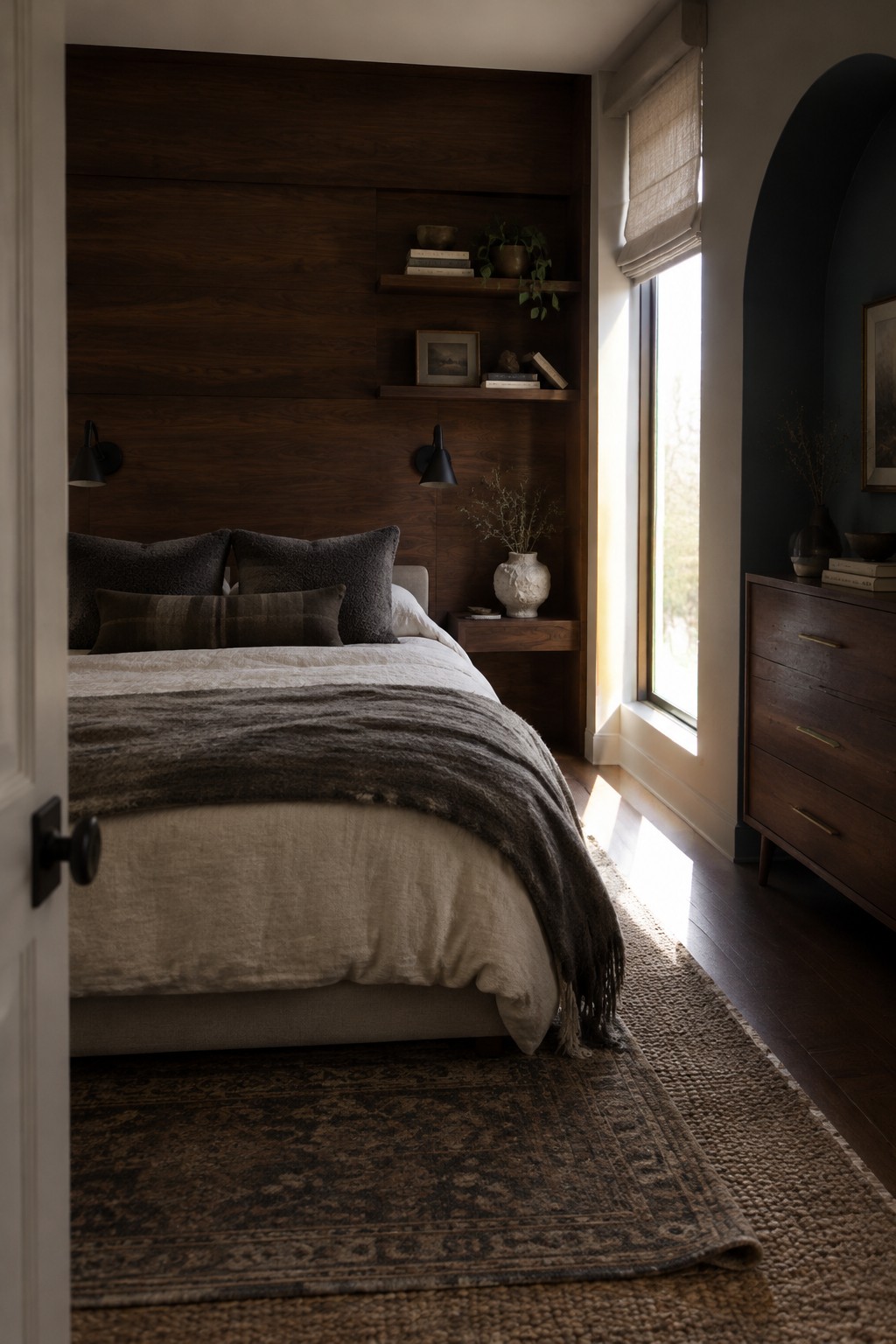 A bedroom with a bed in front of a dark wood paneled wall with floating shelves.