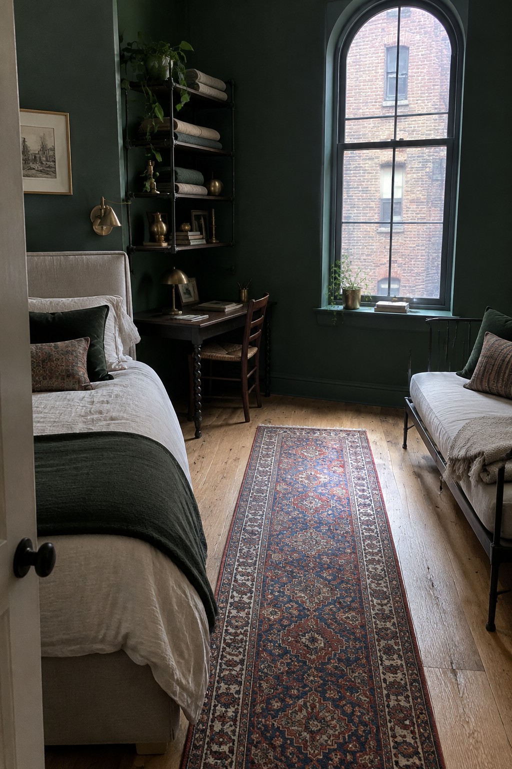 A narrow bedroom with deep green walls, two single beds facing each other, a patterned runner rug, and a tall arched window.