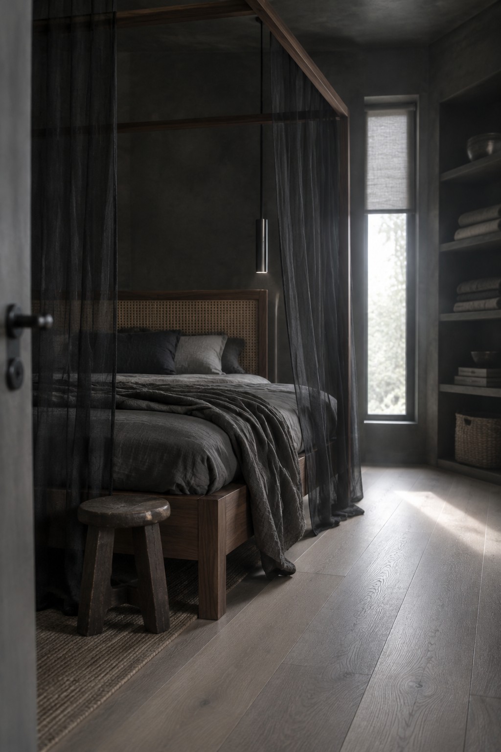 A dark bedroom with a wooden canopy bed, sheer black curtains, gray bedding, and a woven headboard.