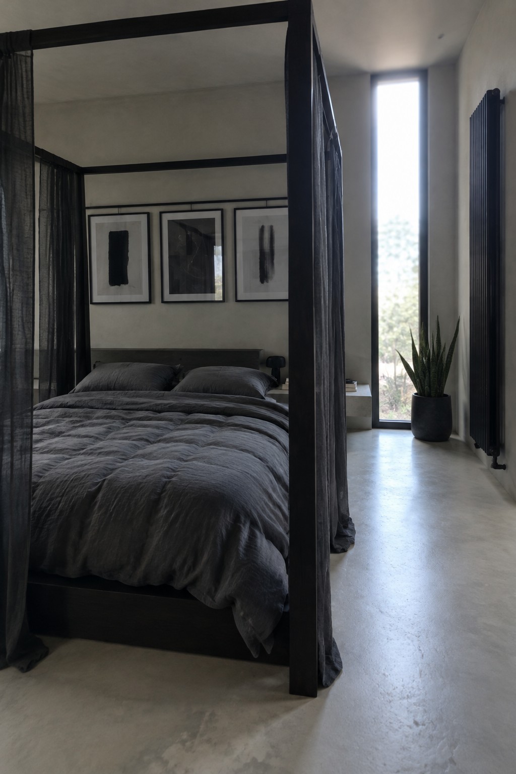 A dark four-poster bed with sheer charcoal curtains, gray bedding, and three framed abstract prints on the wall.