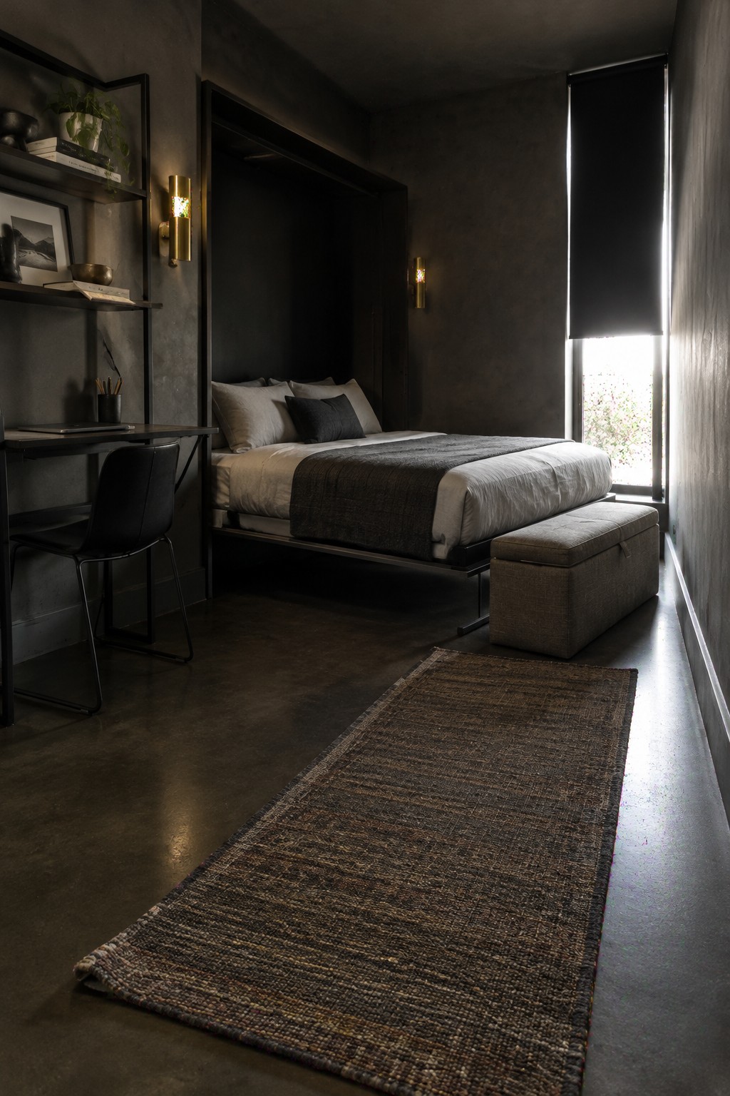 A dark guest bedroom with a bed, a storage bench at its foot, a desk, and a long rug.