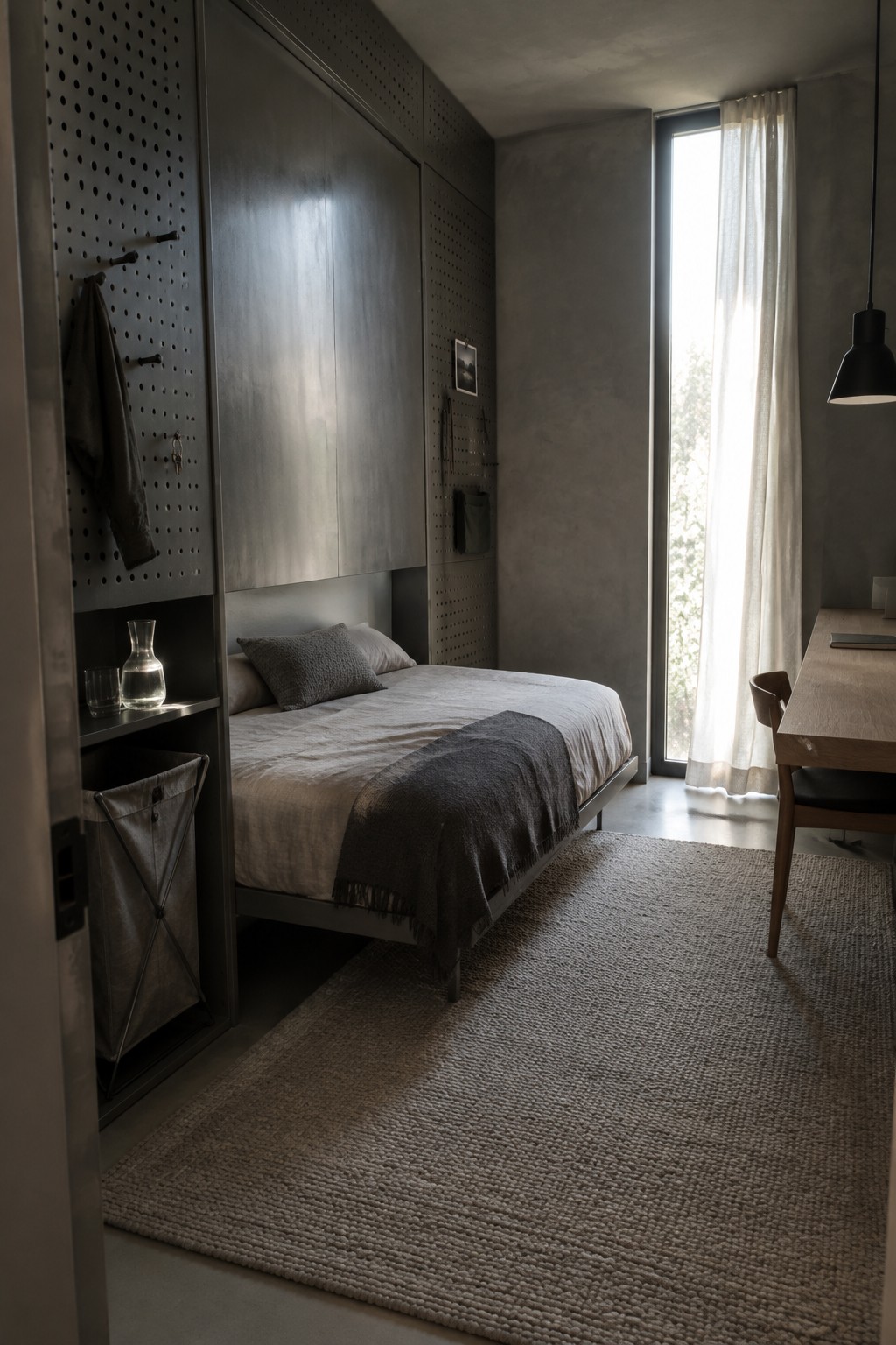 A compact bedroom with a bed built into a tall gray storage wall, perforated panels, and a narrow window with sheer curtains.
