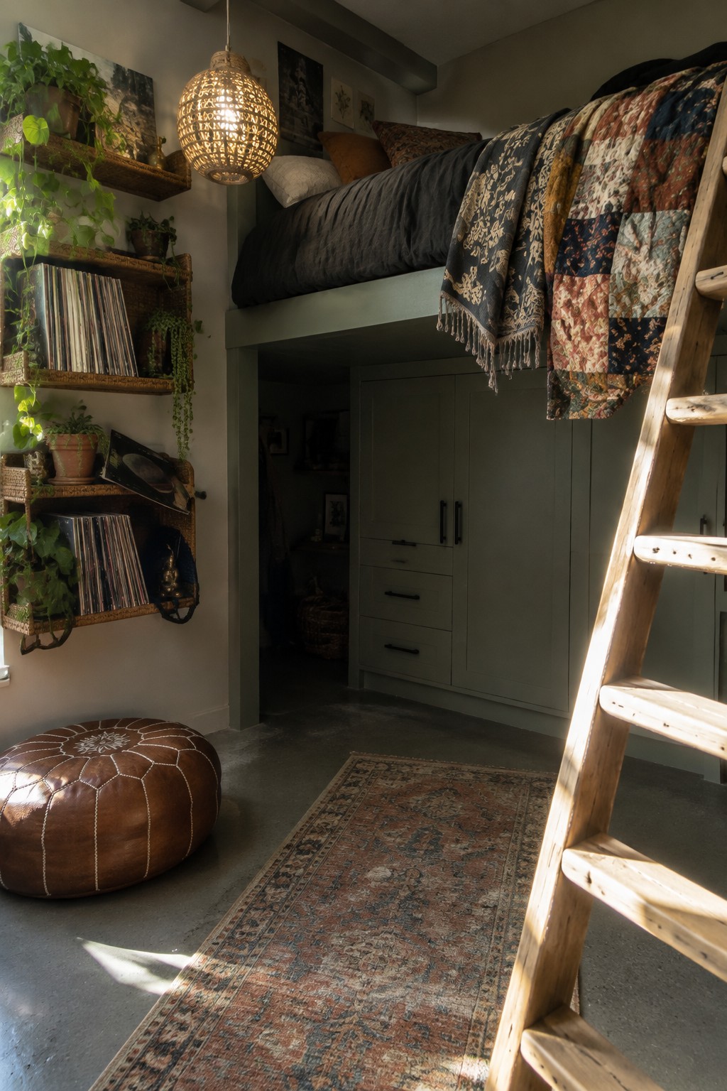 A patchwork quilt hangs over dark bedding on a loft bed, with a wooden ladder beside it.