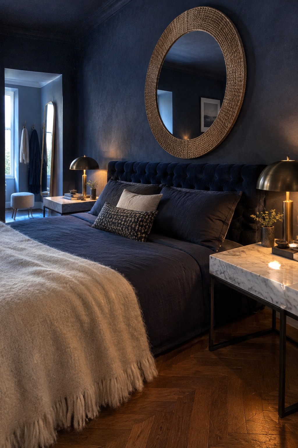 A bedroom with deep navy walls, a dark tufted headboard, and an oval mirror above the bed.
