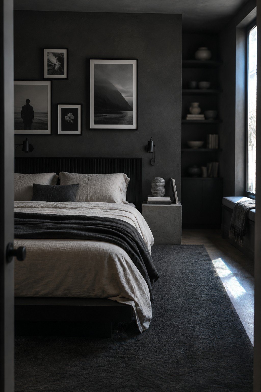 A dark bedroom with a bed, charcoal walls, and a gallery of black-and-white prints above the headboard.